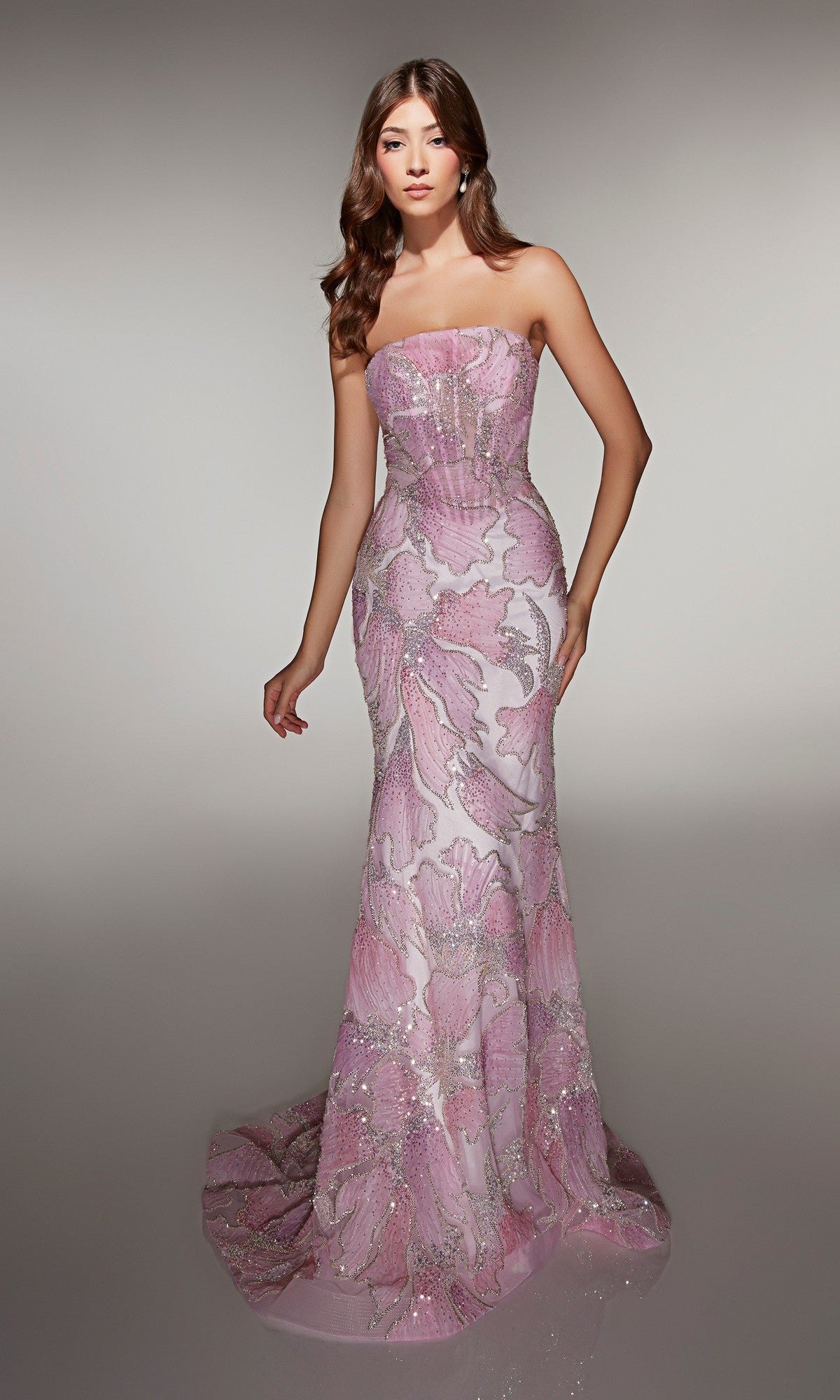 A woman wears the Alyce 62049 long prom dress, a strapless pink and lavender gown with a fitted, floor-length silhouette, sheer corset bodice, beaded embellishments, and floral details, standing against a plain light background.
